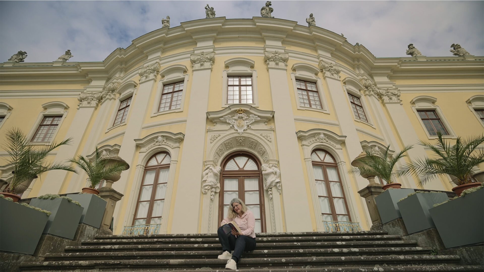 A couple of years_3_2 A woman sitting on the stairs in front of the Ludwigsburg palace. Film still from the documentary "A couple of years".